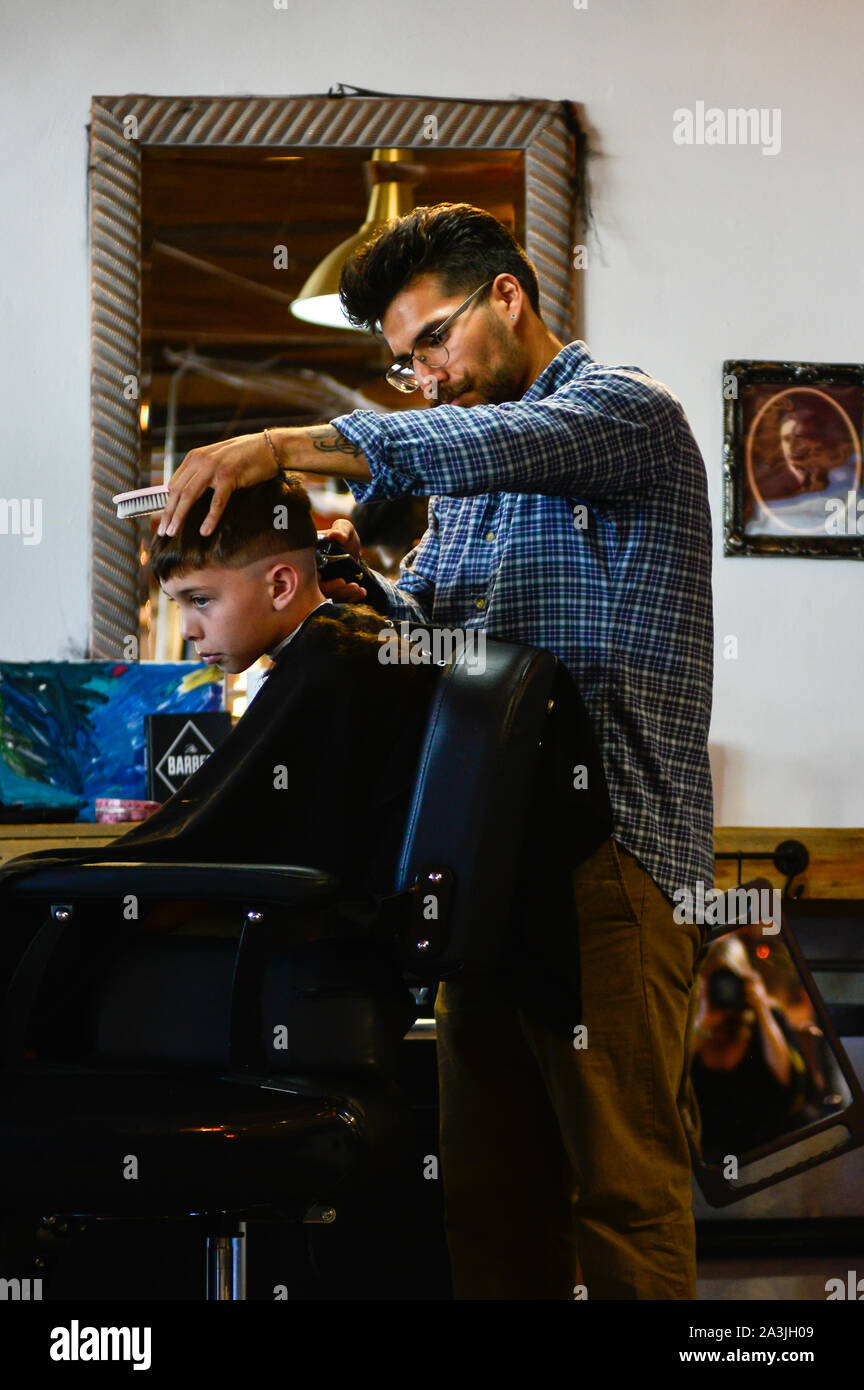 Avec un garçon est assis dans l'aire de coiffeur tout en ayant tendance à coupe de la hanche '81 barbiers shop à Tucson, AZ Banque D'Images