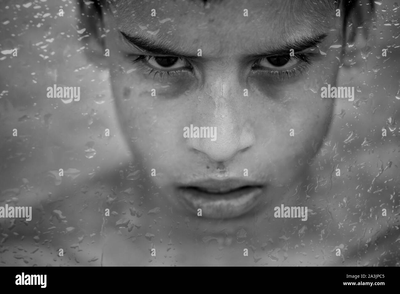 Jeune garçon brésilien derrière la fenêtre couverte de gouttes de pluie Banque D'Images