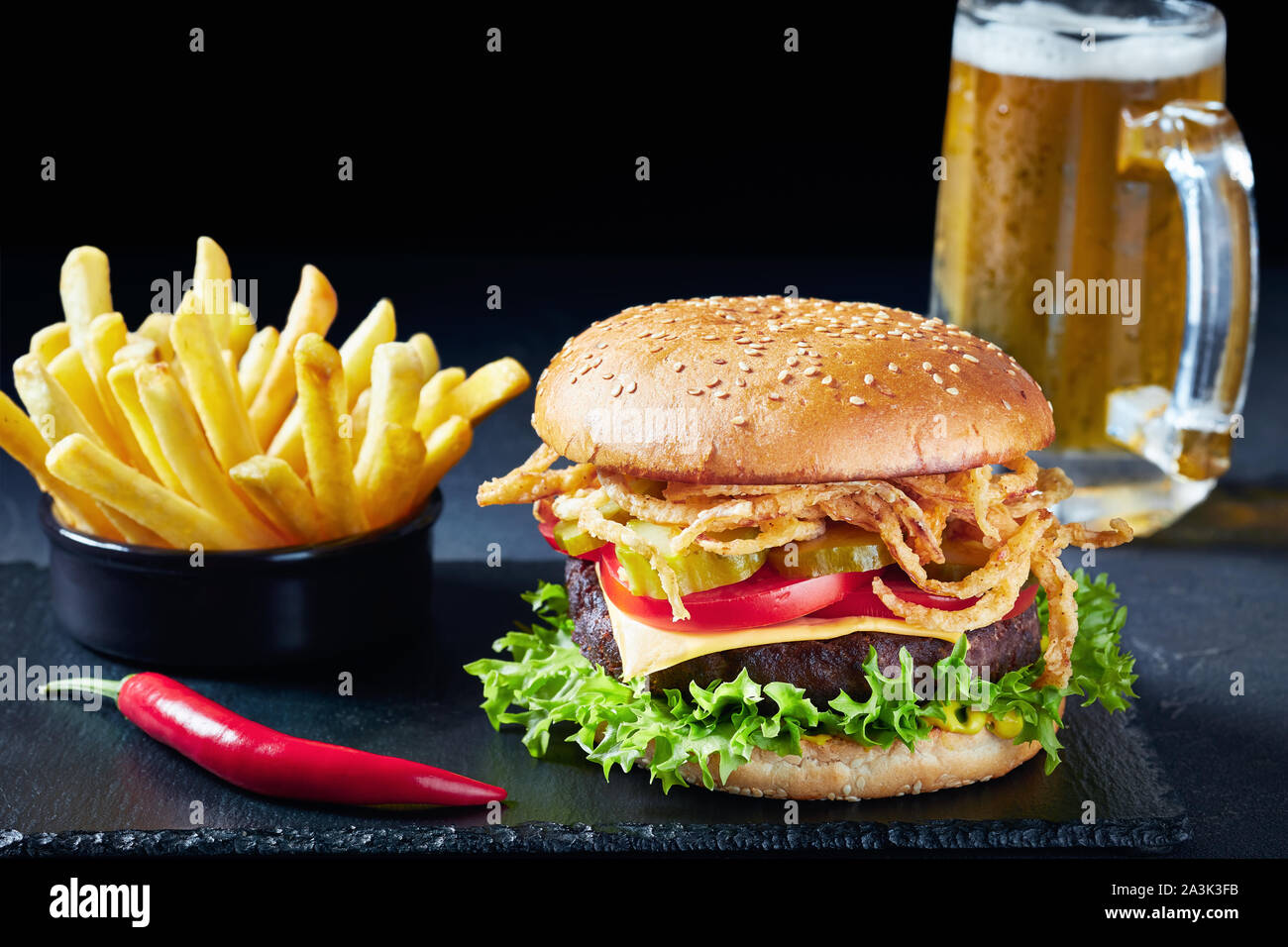 Close-up of Cheeseburger avec Patty de boeuf, cheddar, oignons frits croustillants, laitue, tomates, cornichons sur conseil de pierre avec frites et Banque D'Images