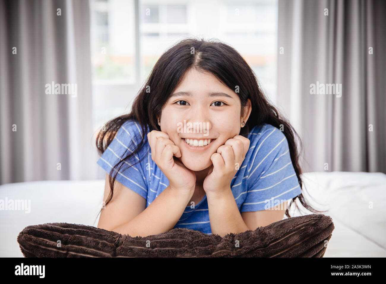 Asian girl jeune adolescente heureuse à la maison chambre à poser sur l'appareil photo lit avec oreiller joyeuse maison de sourire Banque D'Images