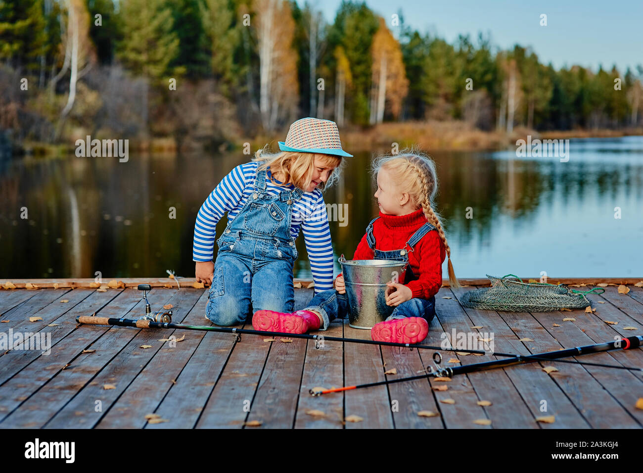 Deux petites sœurs ou vos amis de s'asseoir avec des cannes à pêche sur une jetée en bois. Ils ont attrapé un poisson et le mettre dans un seau. Ils sont heureux avec leurs prises et d Banque D'Images