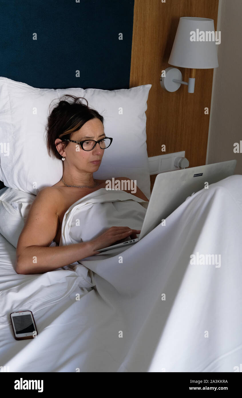 Une femme qui travaille sur son ordinateur tandis que dans le lit. Banque D'Images