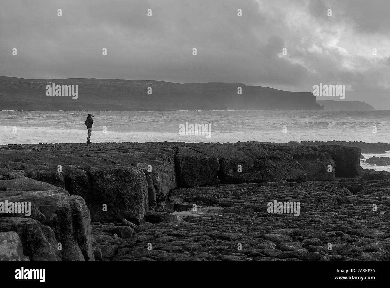 Silhouette d'une jeune femme à Doolin, l'Irlande, avec des falaises à l'arrière-plan. Ciel nuageux au coucher du soleil. Counnty Clare. De gros rochers au premier plan. De l'Atlantique sauvages Banque D'Images