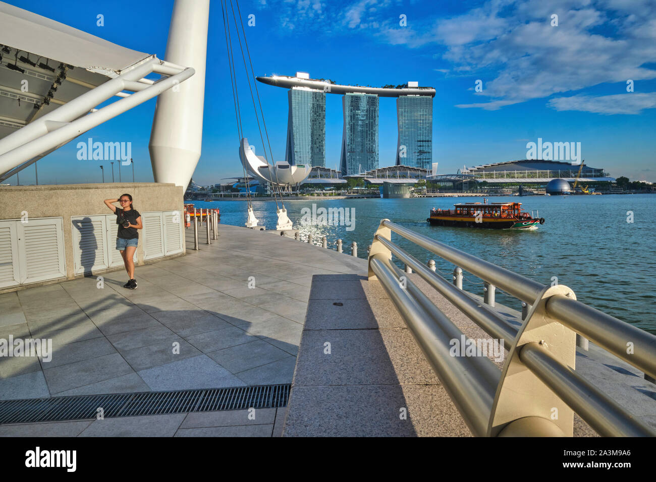 Vue depuis l'Esplanade de Singapour à travers Marina Bay en direction de Marina Bay Sands Hotel et musée ArtScience, avec une jeune fille qui marche par Banque D'Images