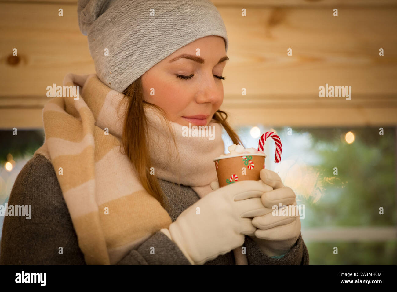 Jeune Femme buvant tasse de chocolat chaud avec de la guimauve en portant  chapeau chaud et écharpe. Assis à côté de fenêtre en cabane en bois  finlandais Photo Stock - Alamy