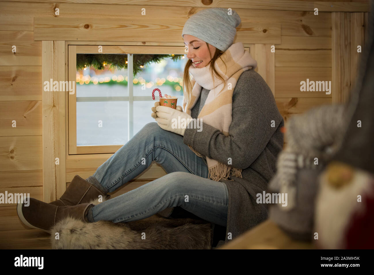 Jeune Femme buvant tasse de chocolat chaud avec de la guimauve en portant  chapeau chaud et écharpe. Assis à côté de fenêtre en cabane en bois  finlandais Photo Stock - Alamy