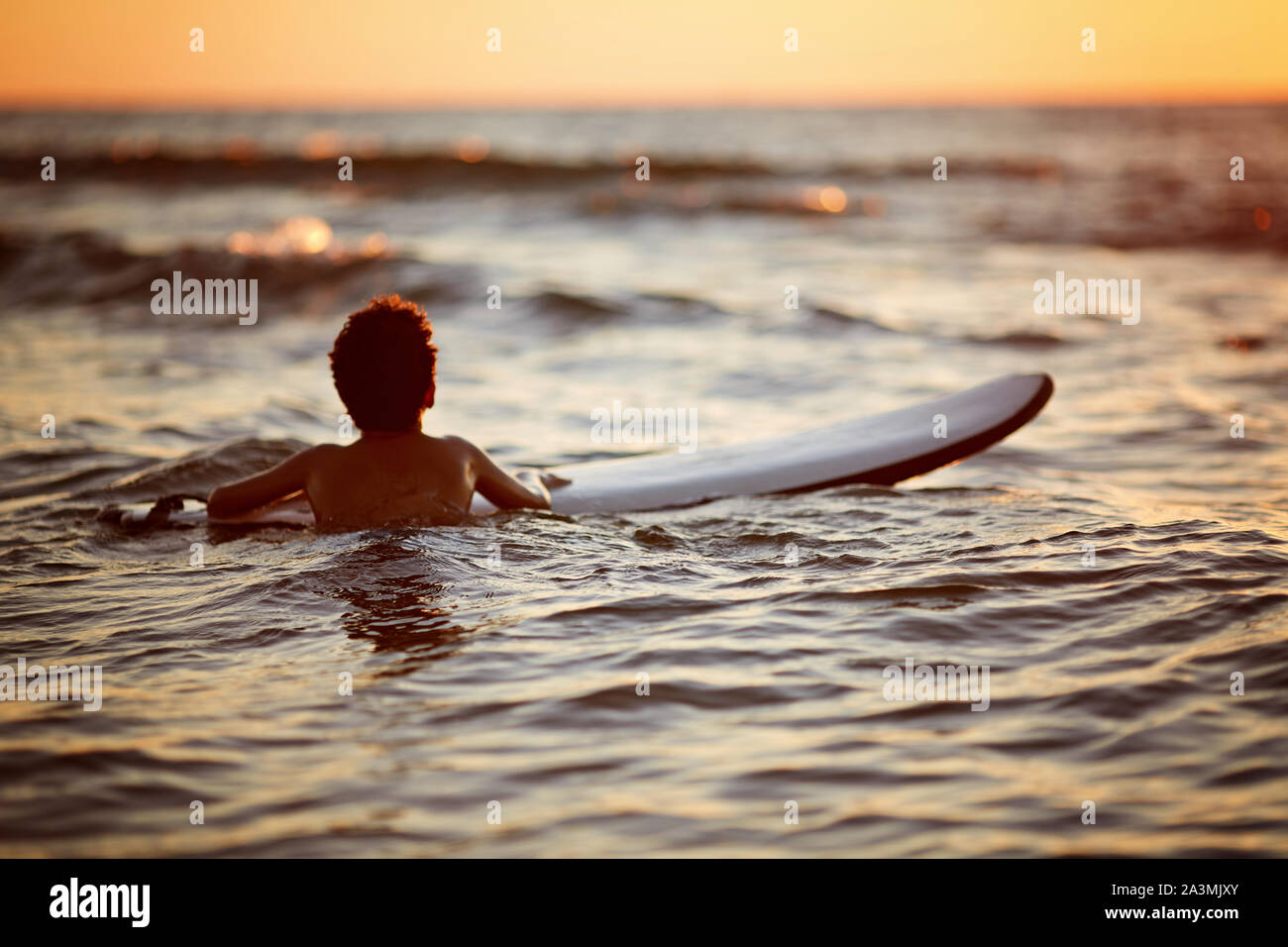 Jeune homme équitation vague au coucher du soleil. Mode de vie actif en plein air. Le surf au coucher du soleil Banque D'Images