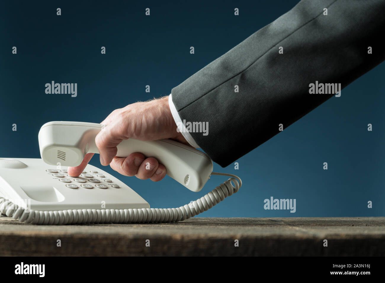 Main d'un businessman holding combiné de téléphone de composer le numéro de téléphone sur blanc téléphone fixe. Sur fond bleu marine. Banque D'Images