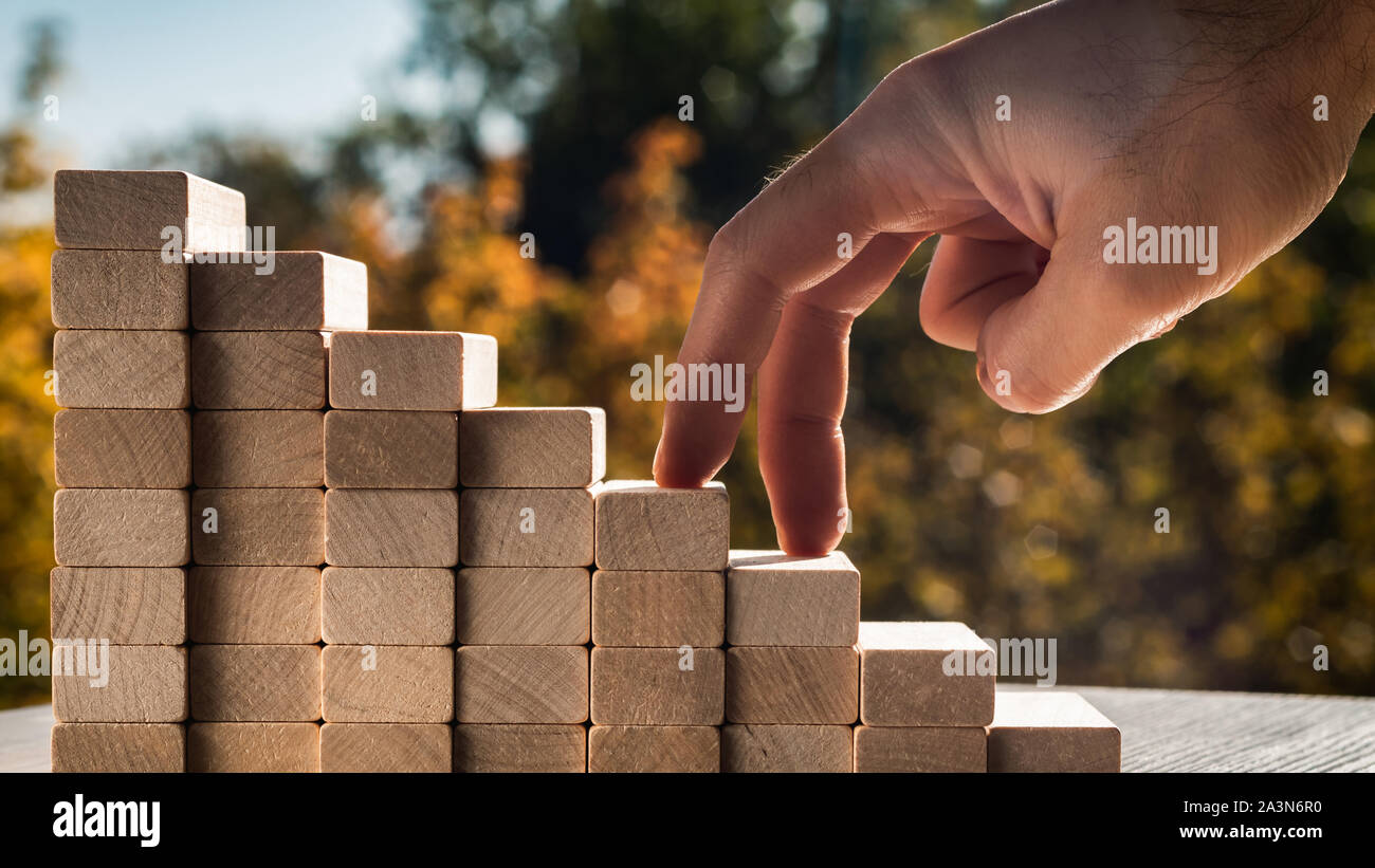 Concept de promotion de l'entreprise objectifs. Les doigts de l'homme monter les escaliers faits de blocs de bois contre l'arrière-plan de feuilles d'automne sur une journée ensoleillée. Banque D'Images