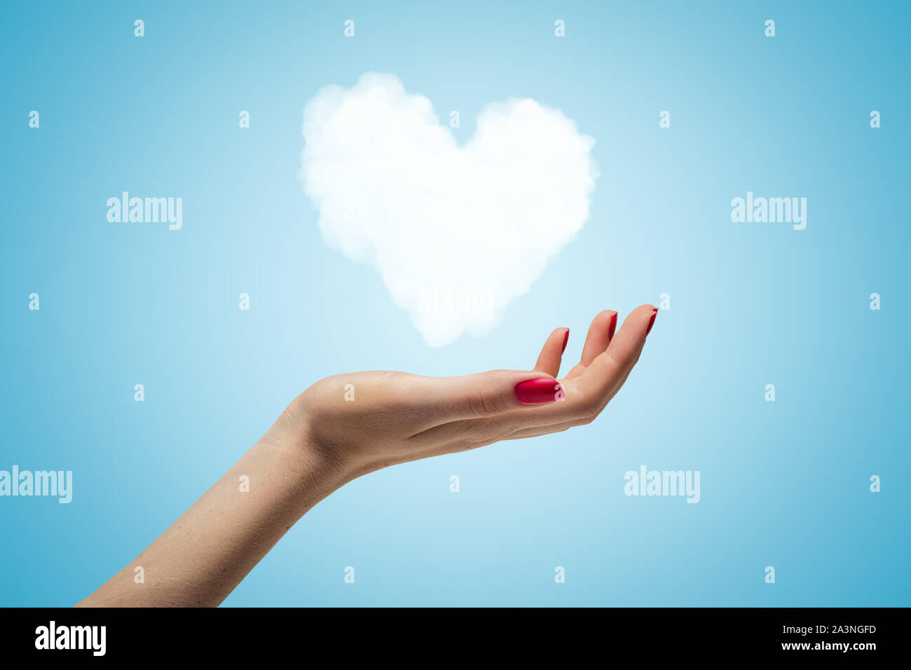 Gros plan du côté de la main de la femme vers le haut et léviter petit nuage en forme de coeur blanc sur fond dégradé bleu clair. Banque D'Images