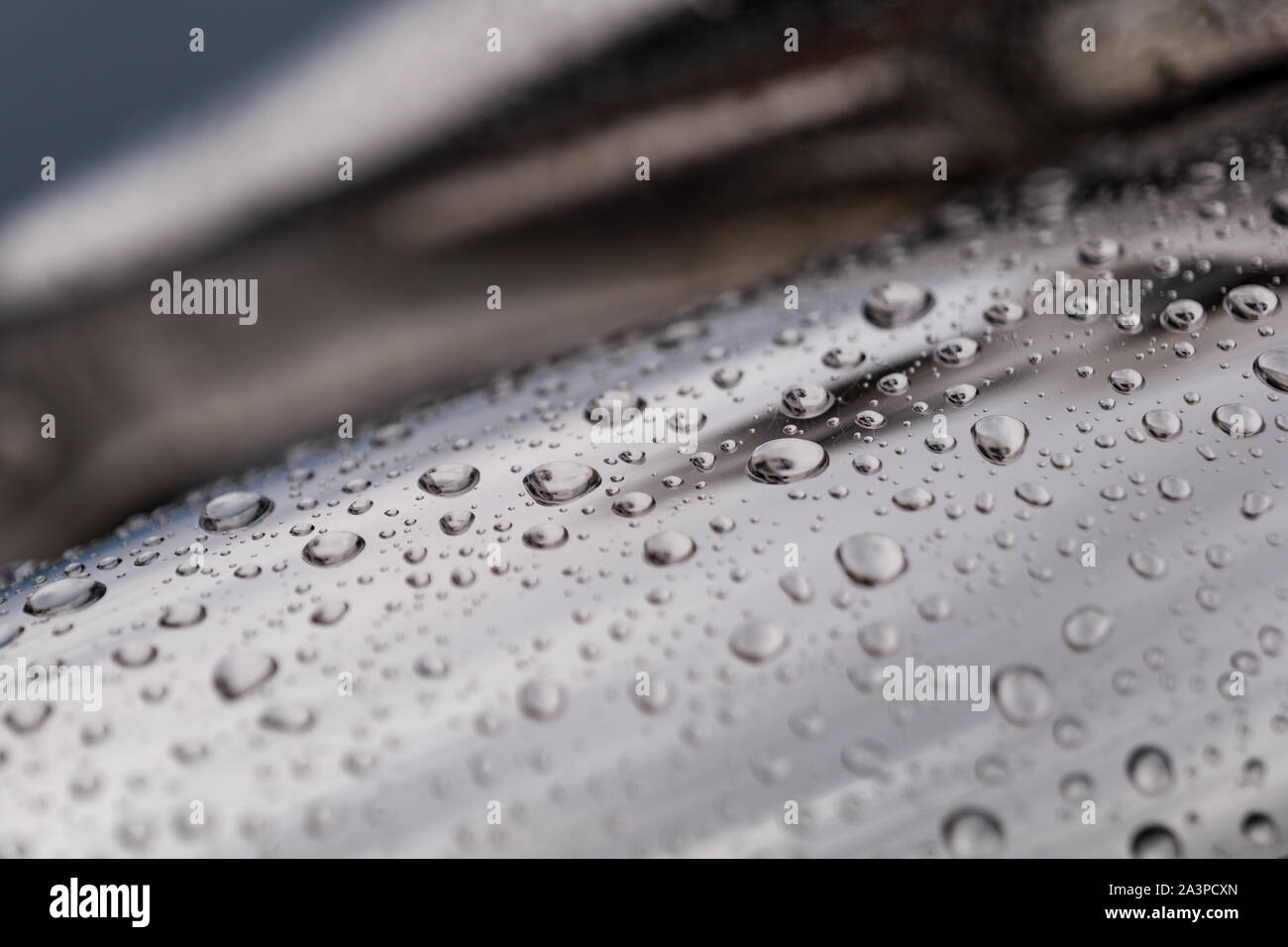 Close up et macro-vision des gouttes d'eau de pluie sur la courbure de la surface chrome brillant et poli de sculpture abstraite. Banque D'Images