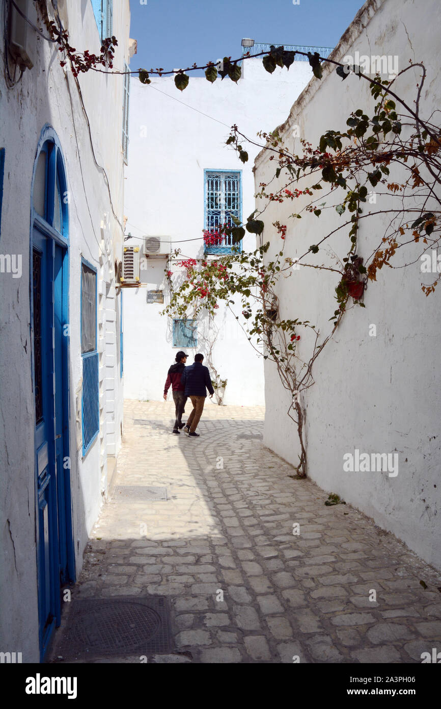 Deux jeunes hommes tunisiens marcher bras dessus, bras dessous dans les rues piétonnes de la Hafsia quart de la médina (vieille ville) de Tunis, Tunisie. Banque D'Images