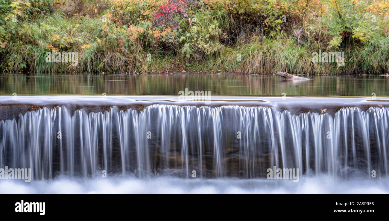 Au cours d'une cascade d'eau sur le barrage de dérivation du fleuve avec poudre de couleur à l'automne en arrière-plan, panorama Banque D'Images