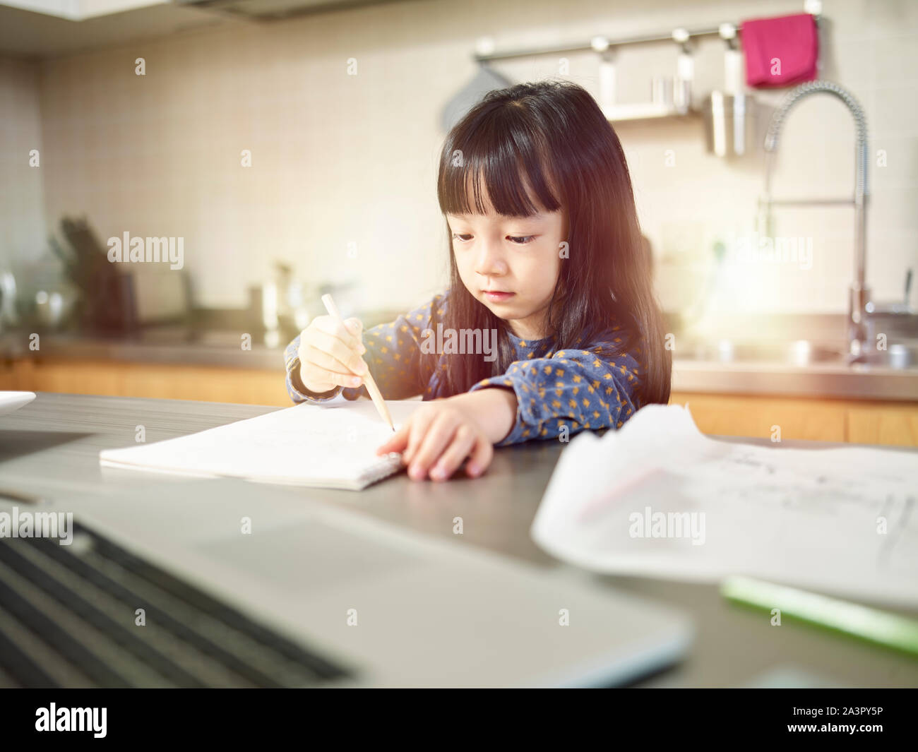 Petite fille asiatique assis au comptoir de la cuisine à la maison faire un dessin. Banque D'Images
