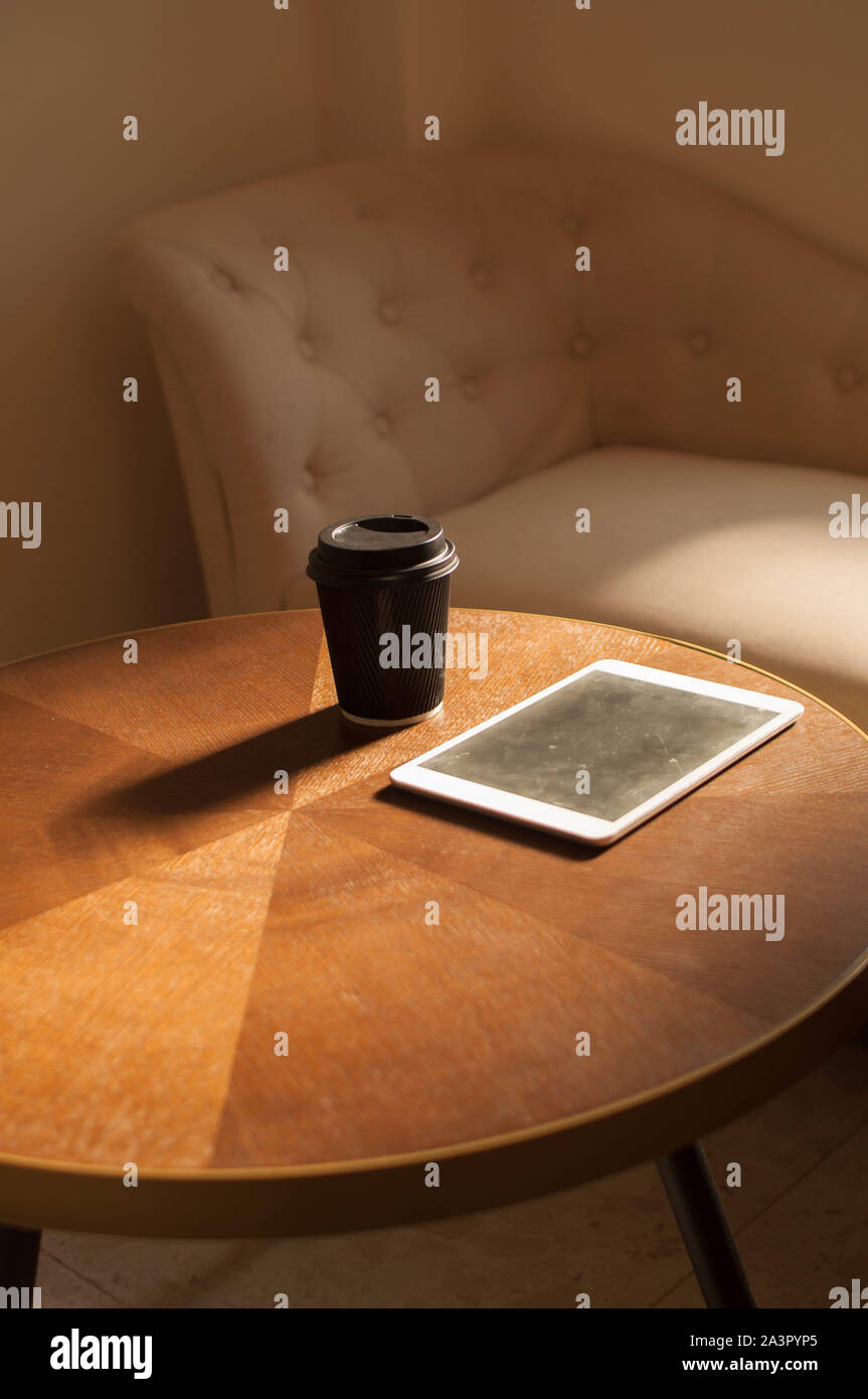 Une tasse de café et une tablette numérique sur une table de bois intérieur avec sunbeam Banque D'Images