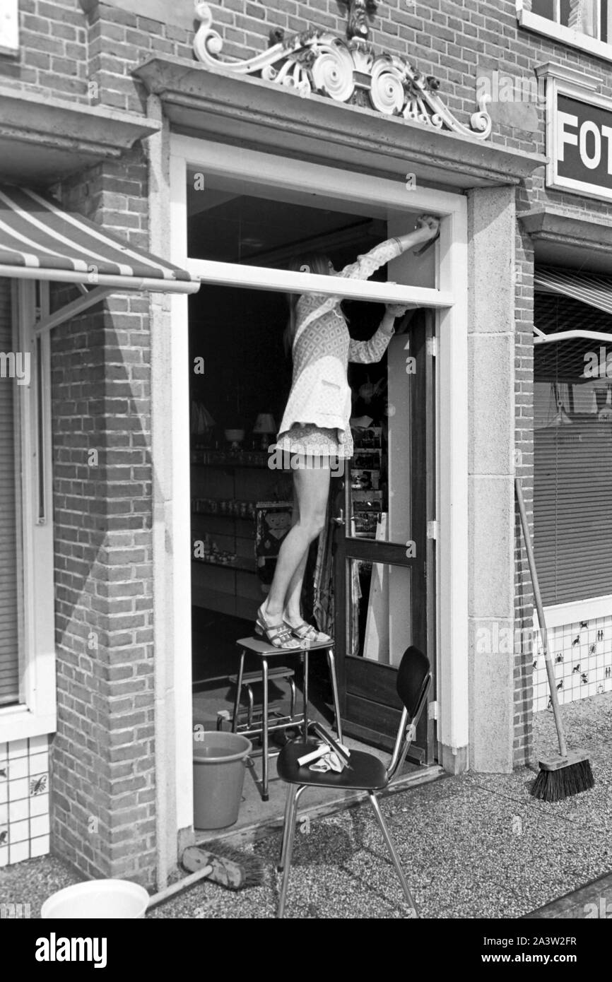 Junge Frau im Minikleid beim Fensterputz in einem Fotogeschäft à Volendam, feuilles en 1971. Jeune femme portant une robe nettoyer les fenêtres d'un atelier photographique à Volendam aux Pays-Bas, 1971. Banque D'Images