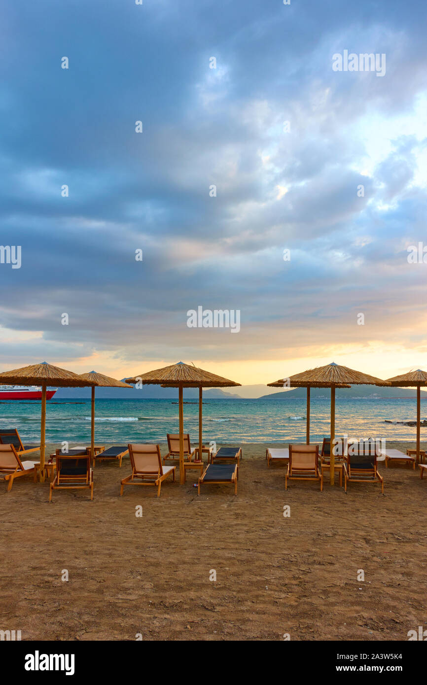 Plage avec chaises-longues et parasols de paille par la mer au coucher du soleil, l'île d'Egine, en Grèce. Composition Copyspace Banque D'Images