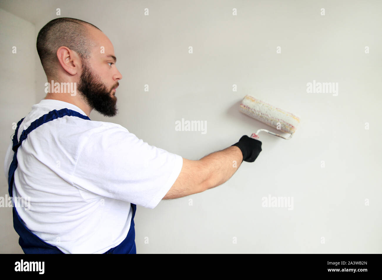 Travailleur de la construction de faire terminer la rénovation à l'appartement. Entrepreneur peintre professionnel à l'aide de la brosse de peinture blanche peinture de mur de béton. Banque D'Images