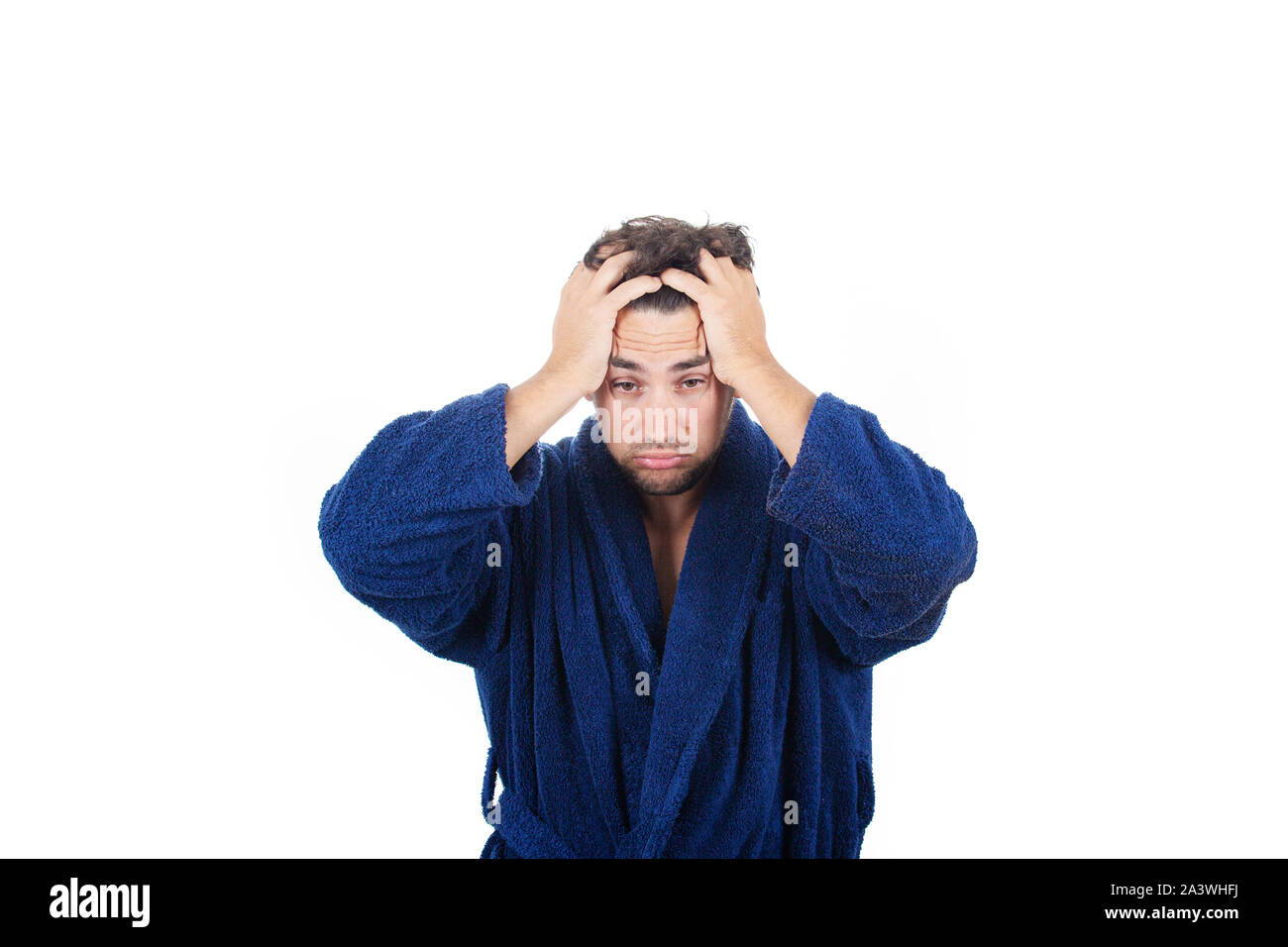 Portrait de jeune homme en retard porte peignoir bleu tenant la main à la tête, incapable de se réveiller à temps pour se rendre au travail, isolé sur fond blanc. Banque D'Images