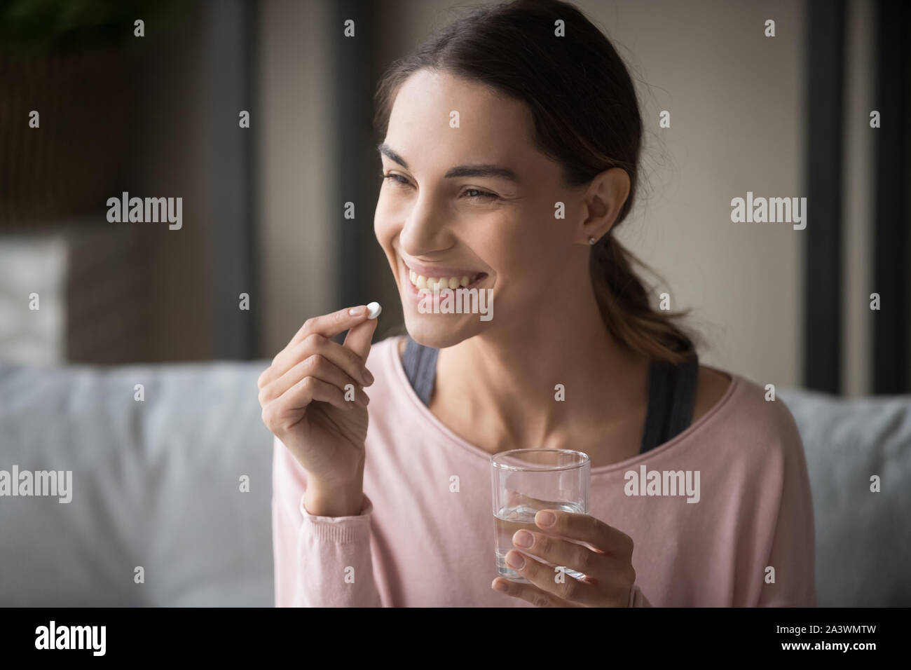 Smiling healthy woman holding pill verre d'eau à la maison Banque D'Images