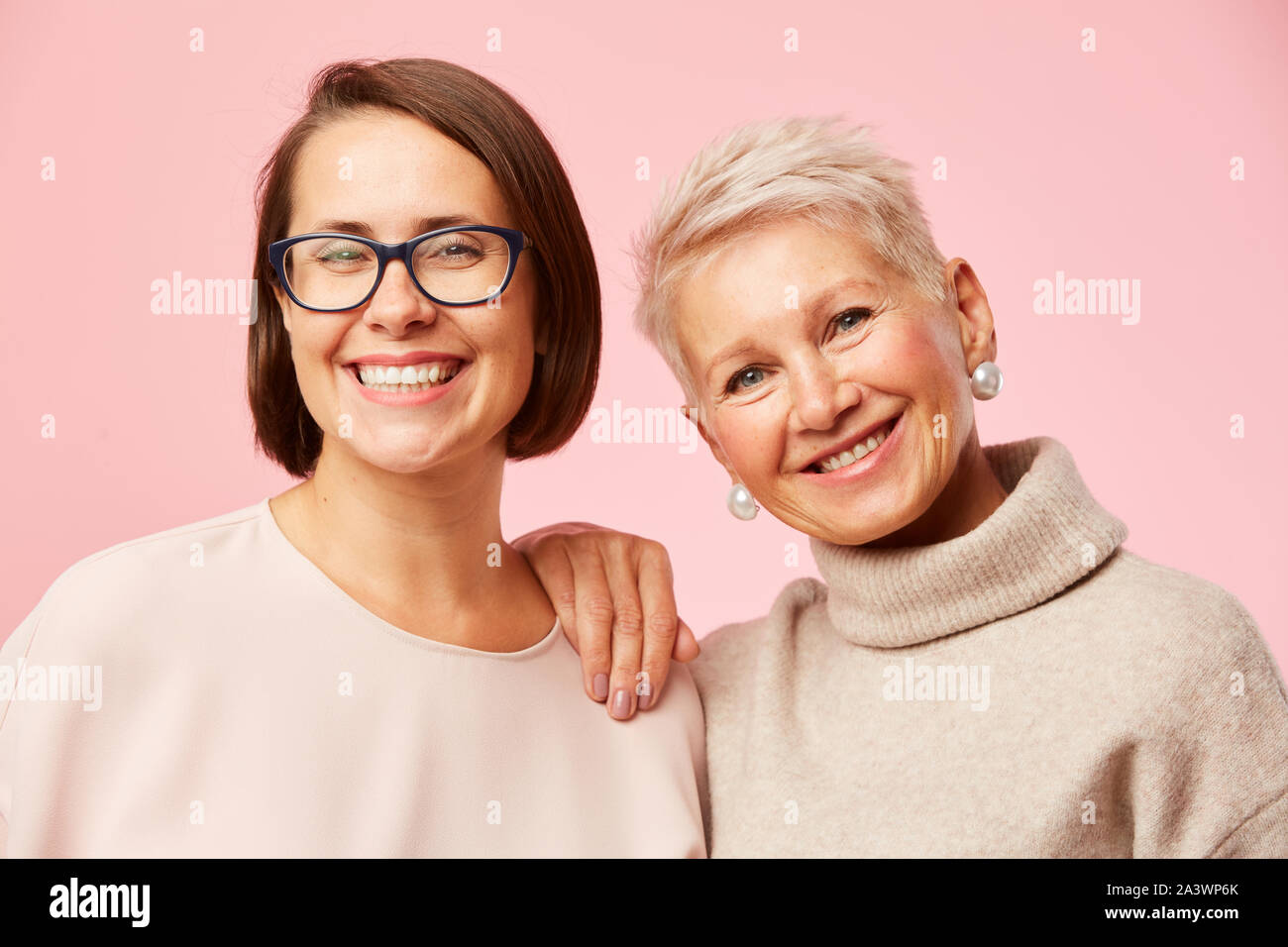 Portrait de belle fille à lunettes se tenant ensemble avec sa mère et ils smiling at camera sur fond rose Banque D'Images