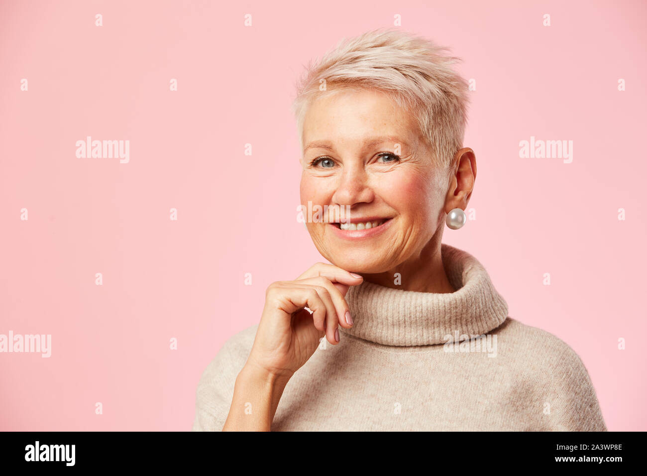 Magnifique Portrait de femme mature avec de courts cheveux blonds smiling at camera isolé sur fond rose Banque D'Images
