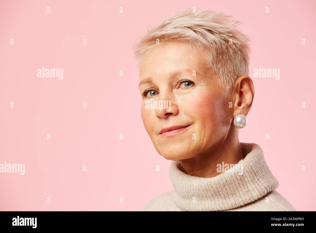 Portrait of senior woman avec des cheveux blonds courts à la caméra à l'encontre de la fond rose Banque D'Images