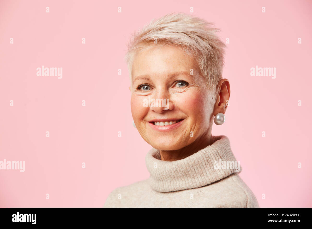 Portrait de femme mature avec de courts cheveux blonds et dans de belles boucles d'smiling at camera sur fond rose Banque D'Images