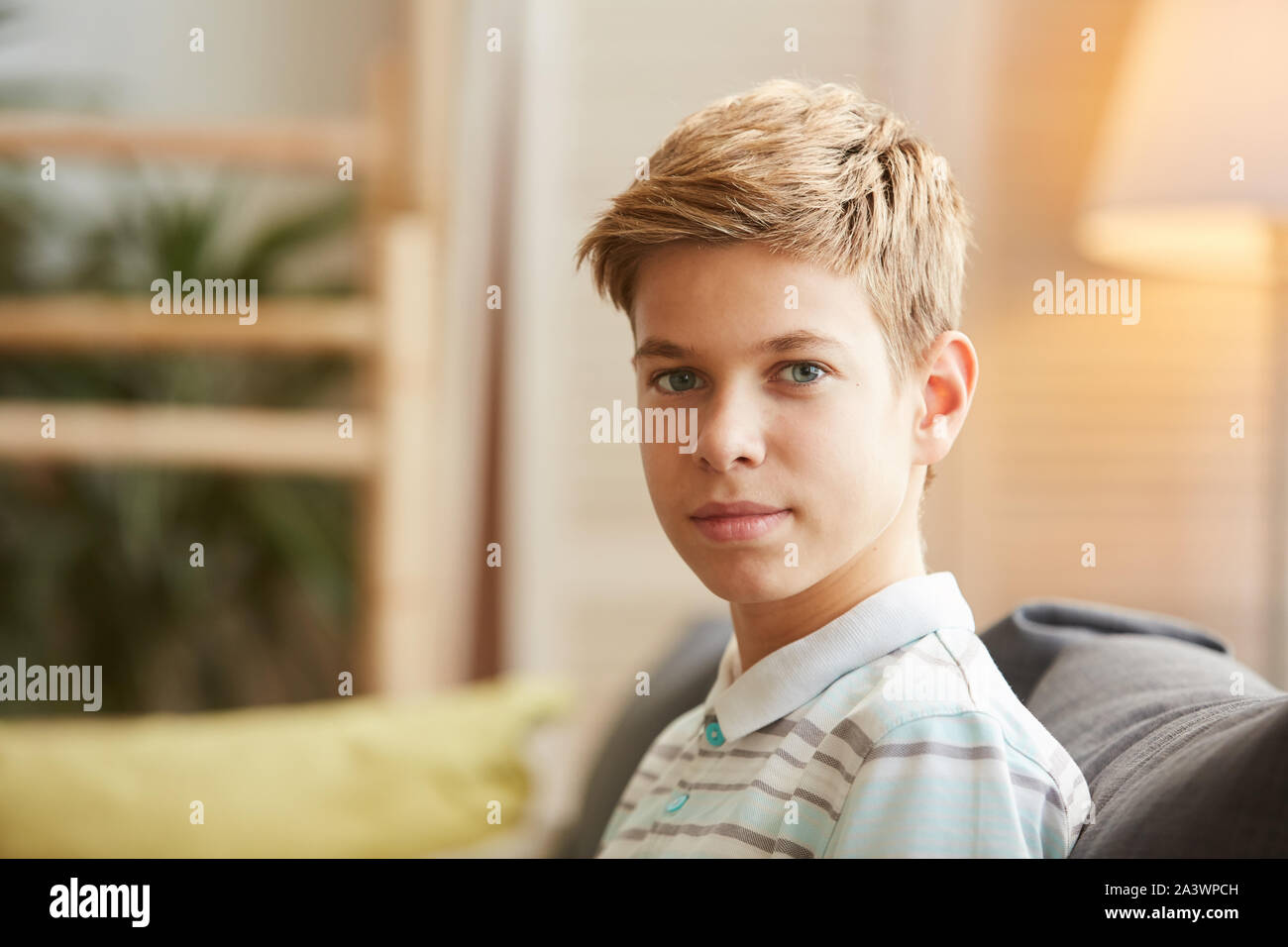 Portrait de jeune garçon aux cheveux blonds looking at camera while sitting on sofa at home Banque D'Images