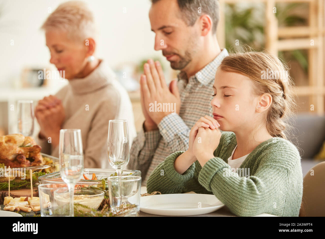 Famille de trois assis à table à manger avec les yeux fermés et prier avant de manger le repas à la maison Banque D'Images