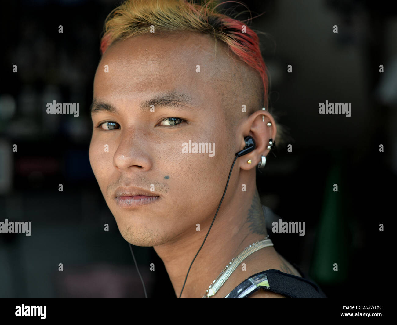 À la cool, jeune homme birman avec écouteurs, les cheveux teints et coupe de cheveux élégante pose pour la caméra. Banque D'Images
