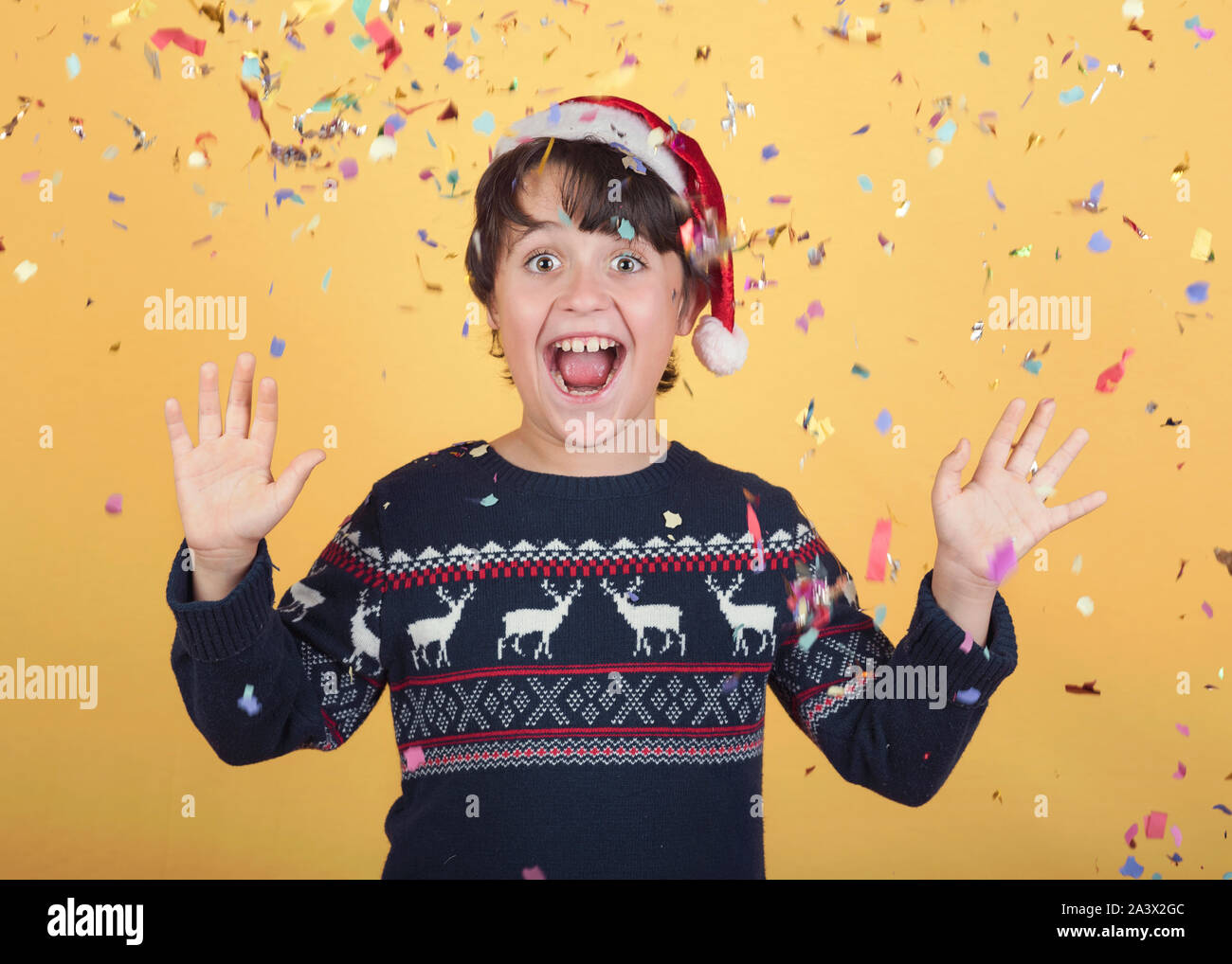 Enfant souriant de confettis Wearing Christmas Santa Claus Hat sur fond jaune Banque D'Images