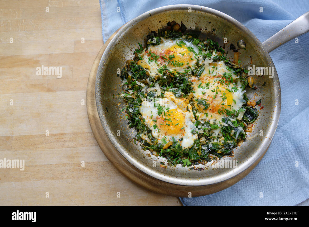 Poêle avec les épinards et œufs frits, d'épices et d'herbes, garnir un plat riche en protéines pour bas régime de carb sur une table en bois, copie espace, high angle de vue de dessus Banque D'Images