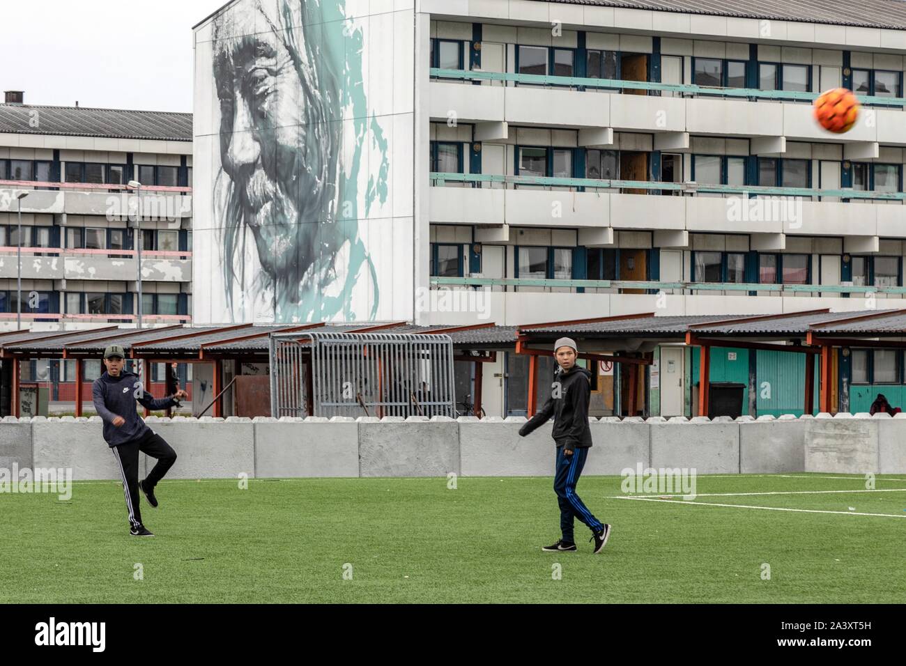 Les jeunes jouent au soccer à l'AVANT DU LOGEMENT SOCIAL PEINTE AVEC LE PORTRAIT D'UN INUIT, Nuuk, Groenland, DANEMARK Banque D'Images