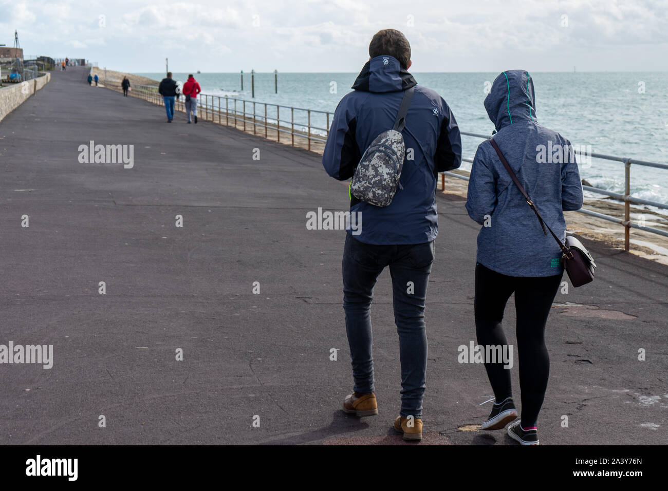 Un couple en train de marcher le long d'une plage par un jour de vent en vêtements d'hiver Banque D'Images