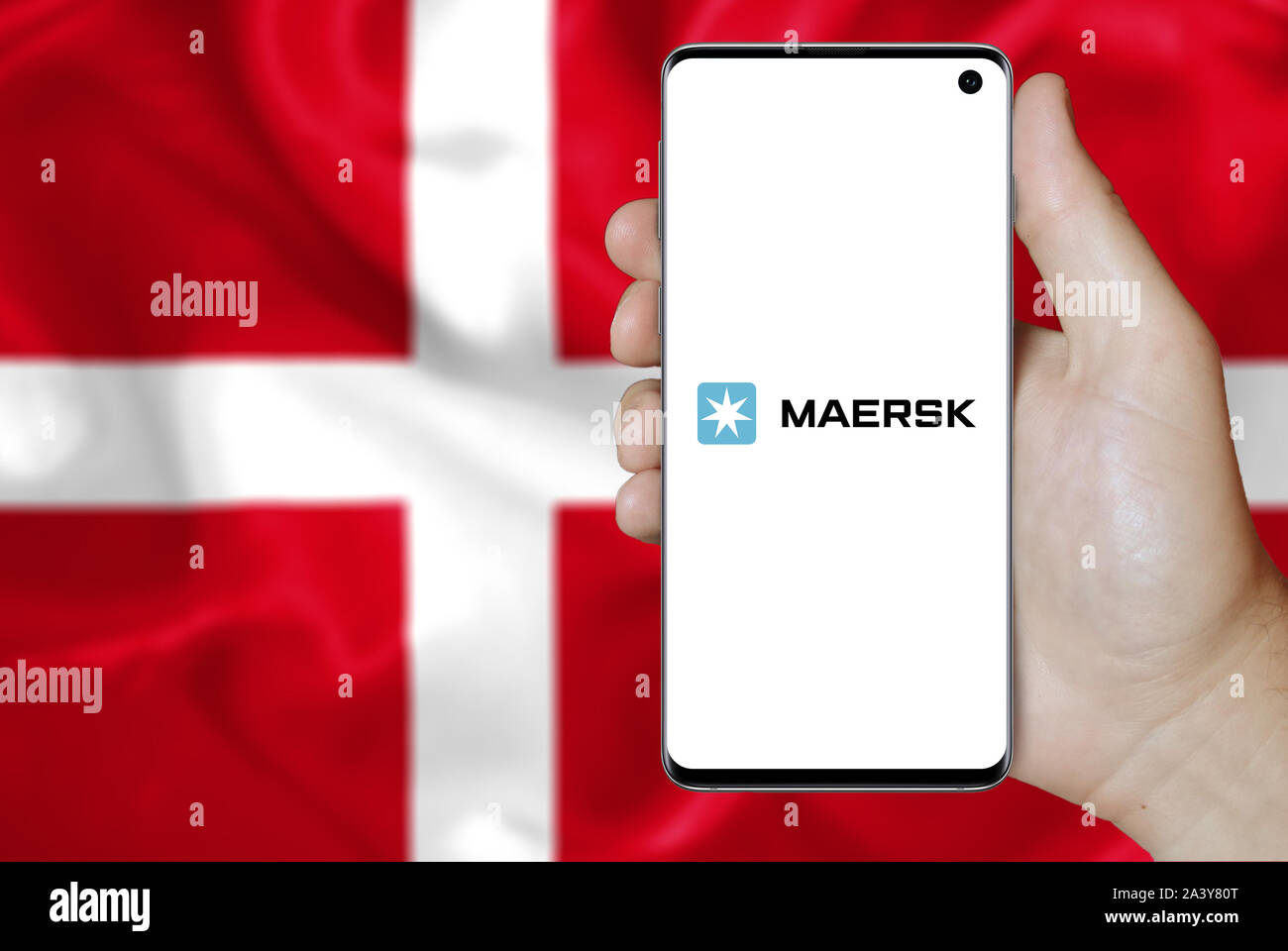 Un homme est titulaire d'un téléphone d'afficher le logo de société A.P. Møller - Maersk énumérés sur l'OMX Copenhagen. Drapeau danois arrière-plan. Credit : PIXDUCE Banque D'Images