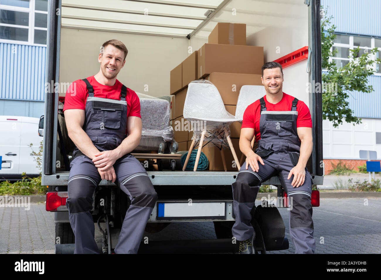 Portrait Of Smiling Movers assis en Van avec pile de cartons et de meubles Banque D'Images