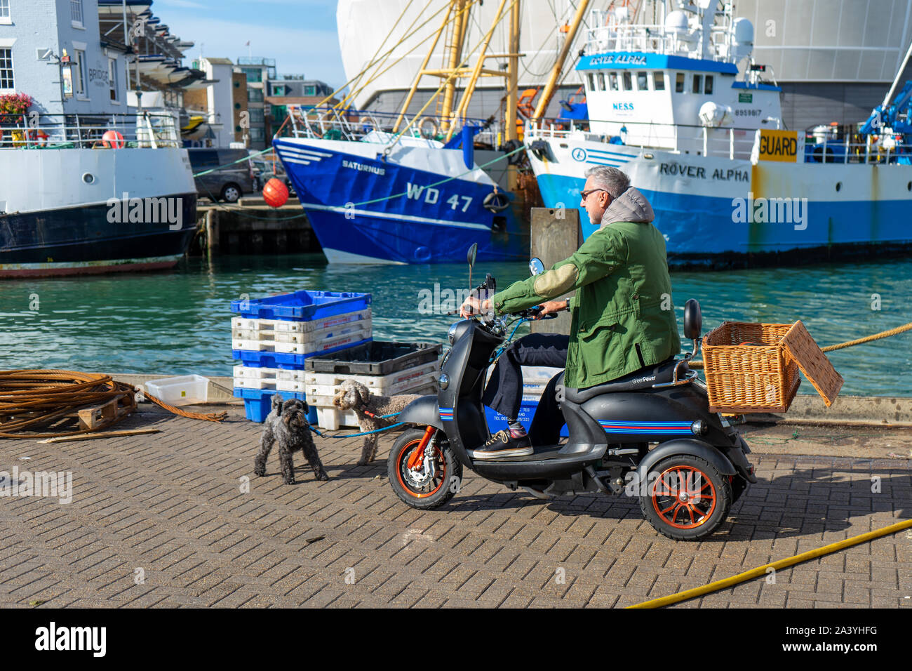 Un homme d'âge moyen sur un scooter de mobilité en tenant son chien pour une promenade sur le quai ou le dock Banque D'Images