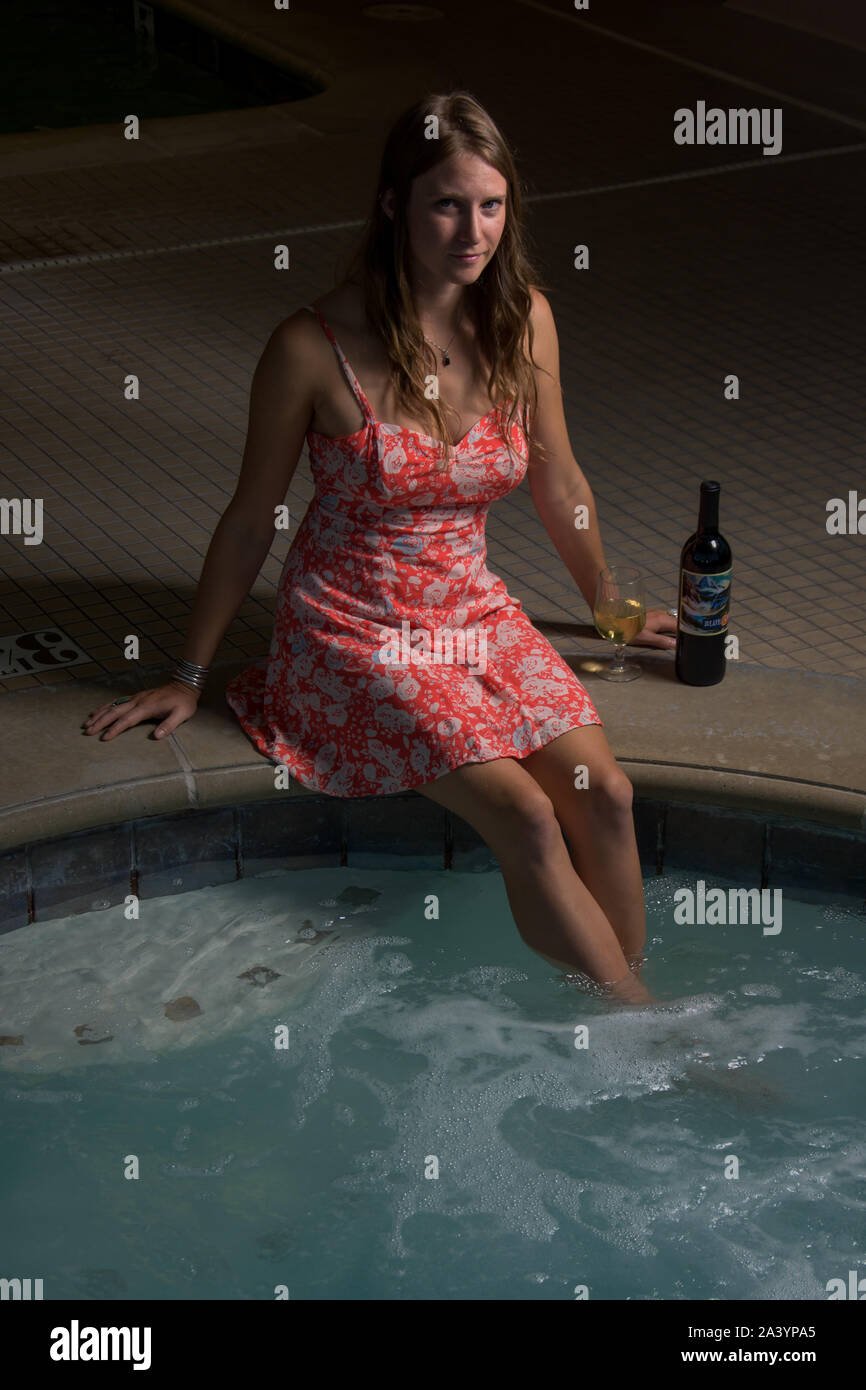 Une jolie jeune femme imbibe ses pieds et jambes en buvant de l'alcool dans un bain à remous pour se détendre et de stress après le travail. Banque D'Images