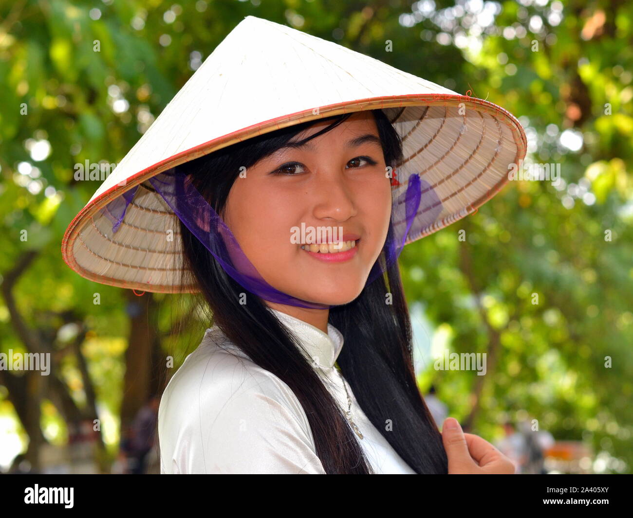Belle et jeune femme wearsan vietnamienne asiatique élégant chapeau de paille conique (nón lá) avec mentonnière en soie bleu et sourit pour la photo. Banque D'Images