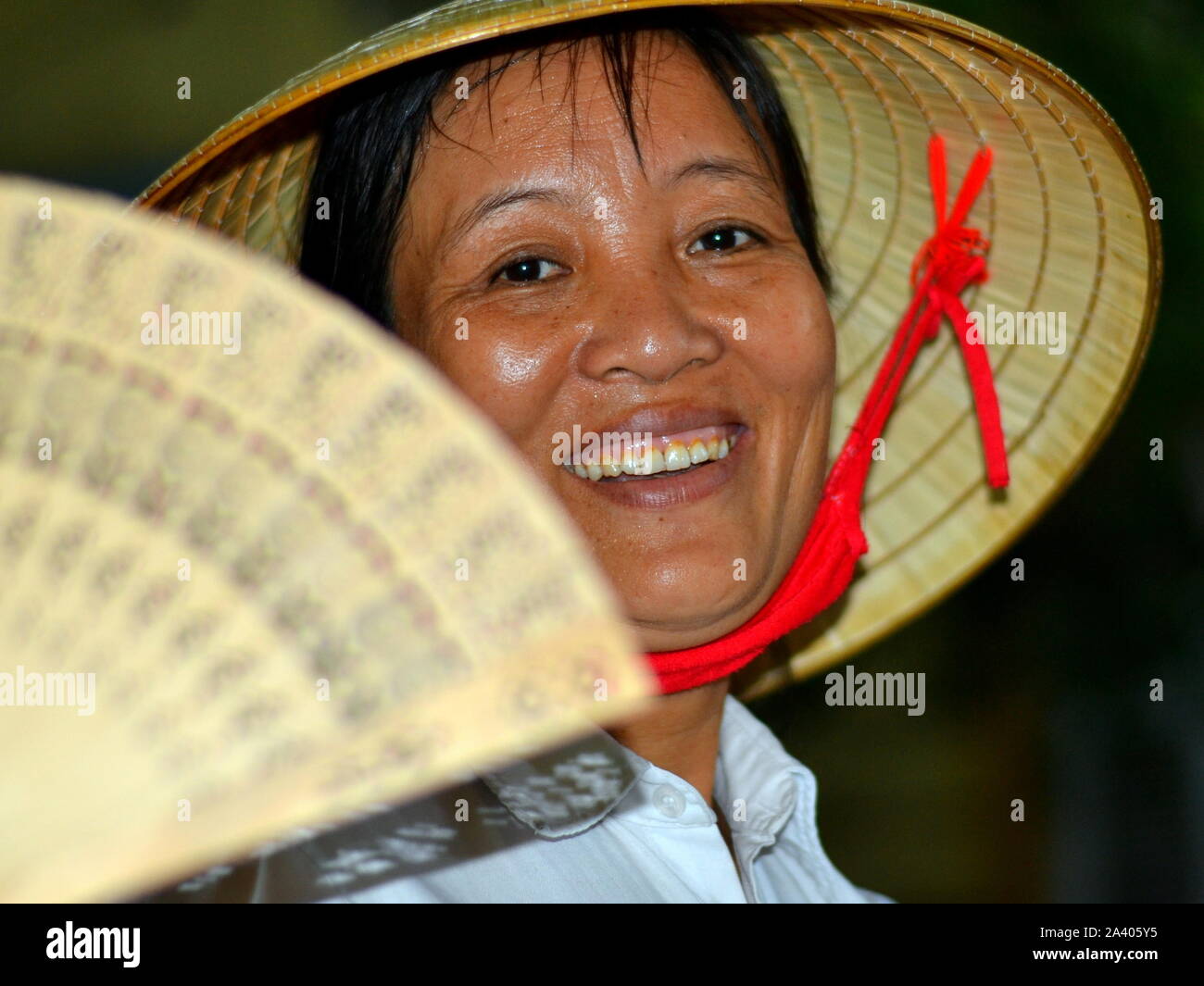 La sudation vietnamienne porte un chapeau de paille conique asiatiques (nón lá) avec du tissu rouge jugulaire et sourit pour la photo. Banque D'Images