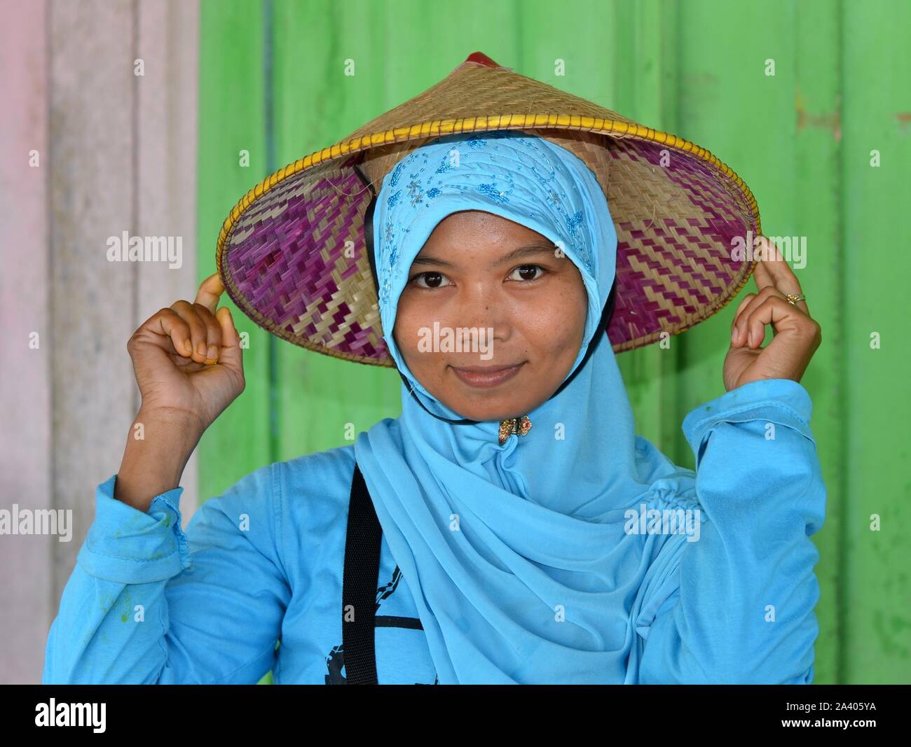Jeune femme musulmane indonésienne porte sur le dessus de son hijab turquoise un chapeau de paille conique asiatiques (caping) avec appuie-tête. Banque D'Images