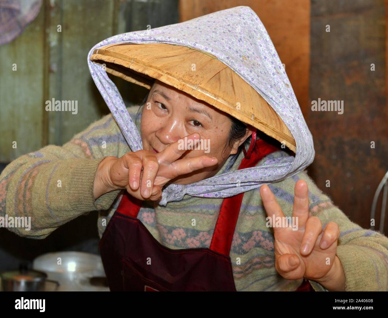 Vendeur de rue taiwanais âgés asiatique porte un chapeau de paille conique (dǒulì) chiffon avec mentonnière et clignote le double v signe avec les deux mains. Banque D'Images