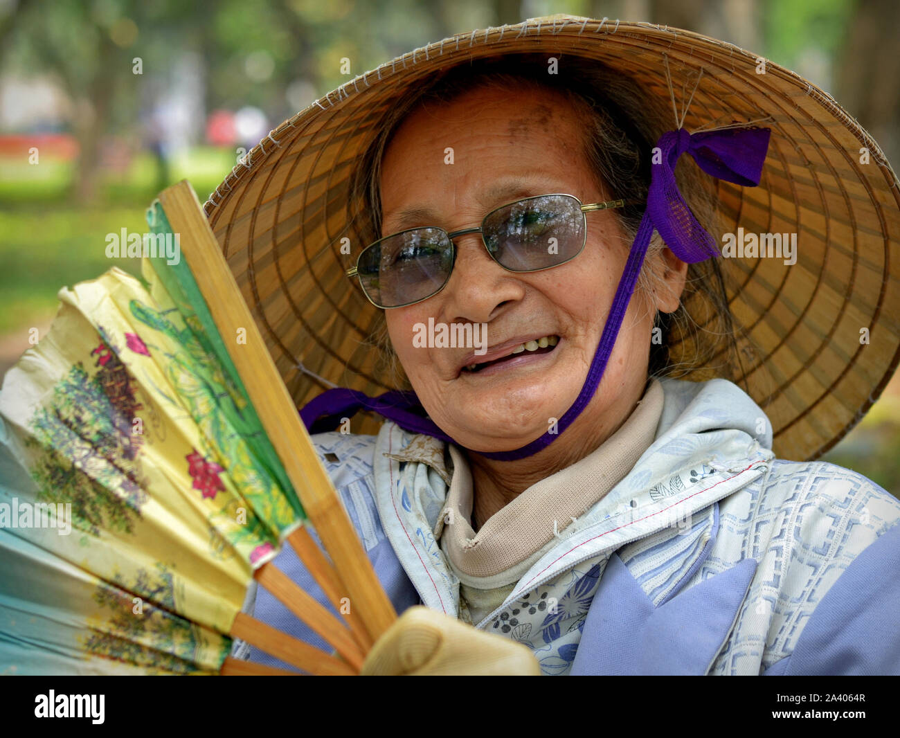 Personnes âgées vietnamienne avec chapeau conique asiatique pose pour l'appareil photo avec un ventilateur de poche traditionnel bambou. Banque D'Images