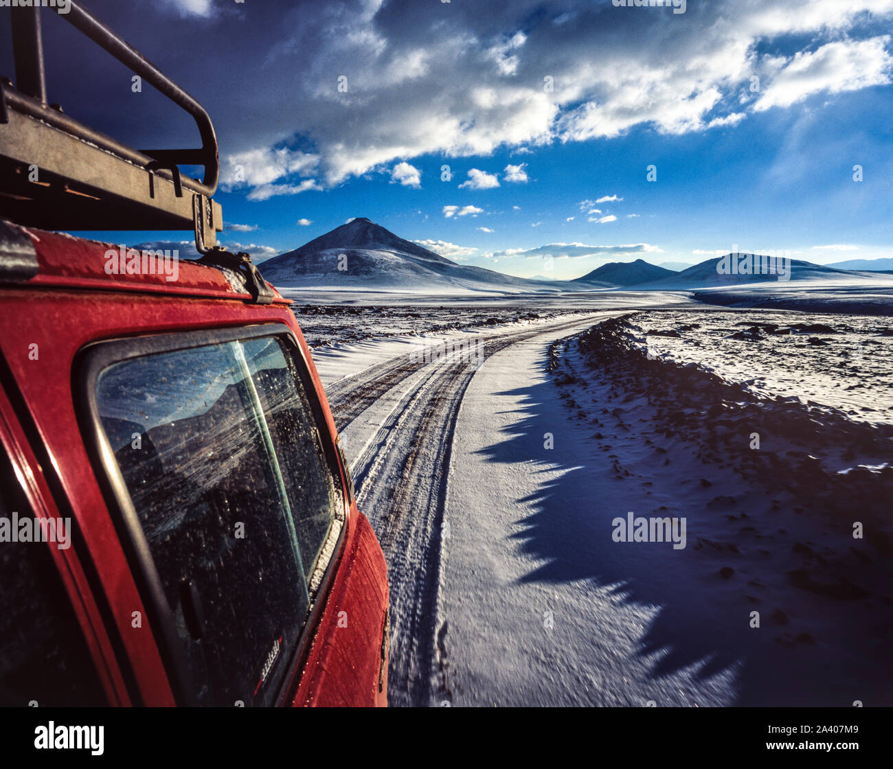 Jeep rouge roulant le long d'un chemin couvert de neige sur l'Altiplano en Bolivie, avec des montagnes en arrière-plan Banque D'Images