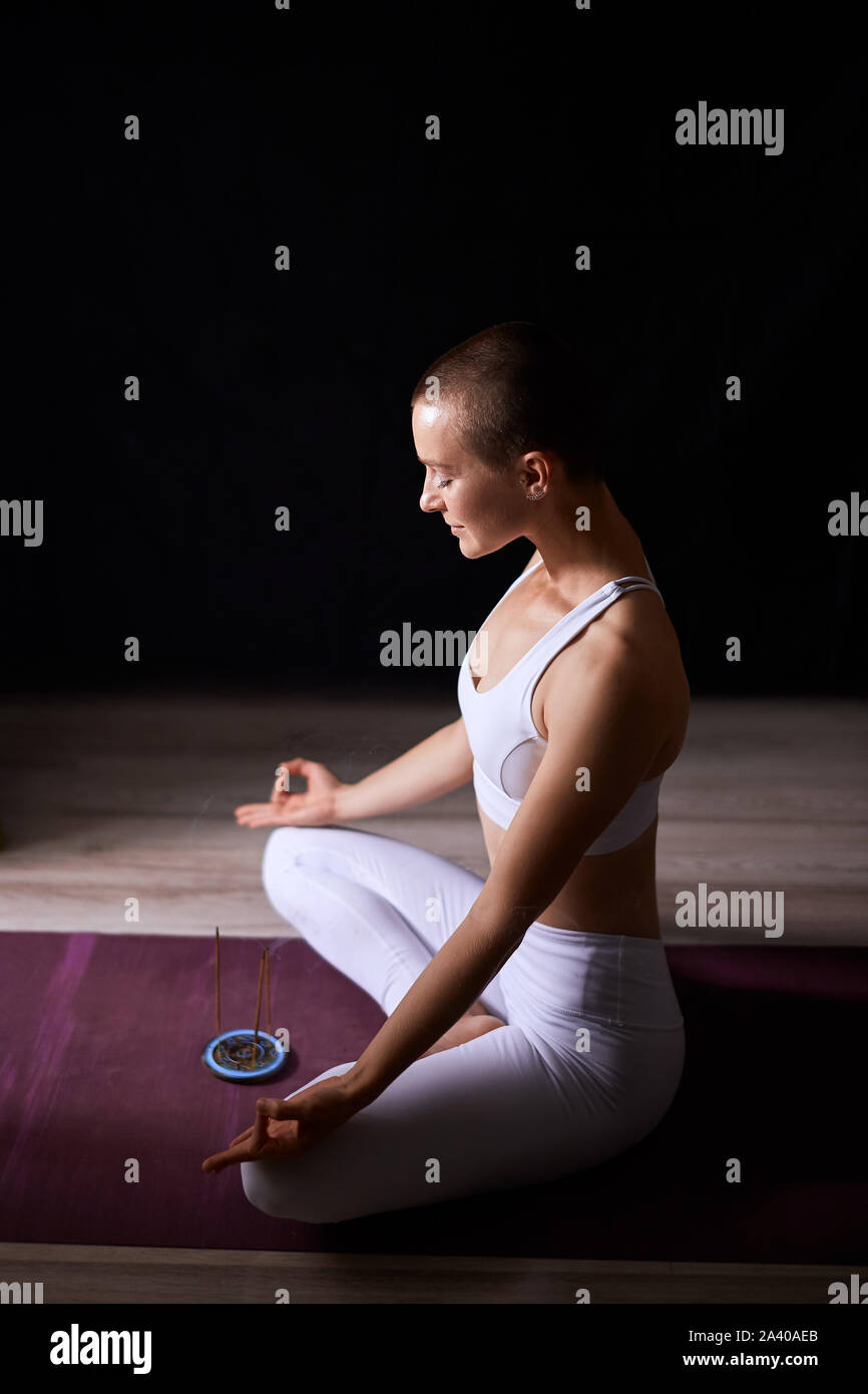 Short-haired woman s'asseoir en lotus constituent et de méditer. La méditation de yoga. Fond noir Banque D'Images