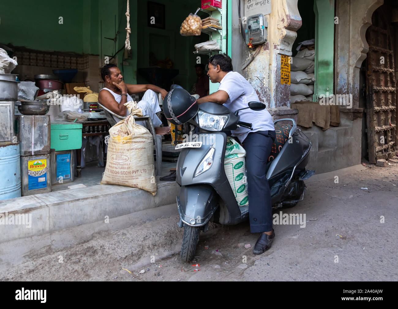 L'homme indien sur un scooter de parler à un vendeur du magasin d'épices, du Rajasthan, Jodhpur, Inde Banque D'Images