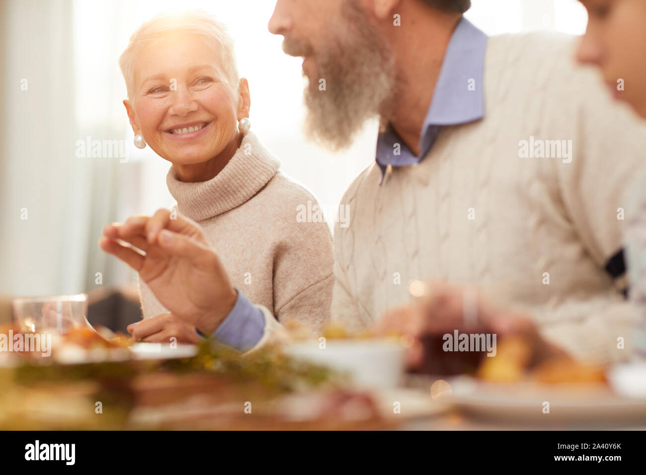 Femme mature avec de courts cheveux blonds en souriant à l'homme tout en parlant de lui à la table pendant le dîner Banque D'Images