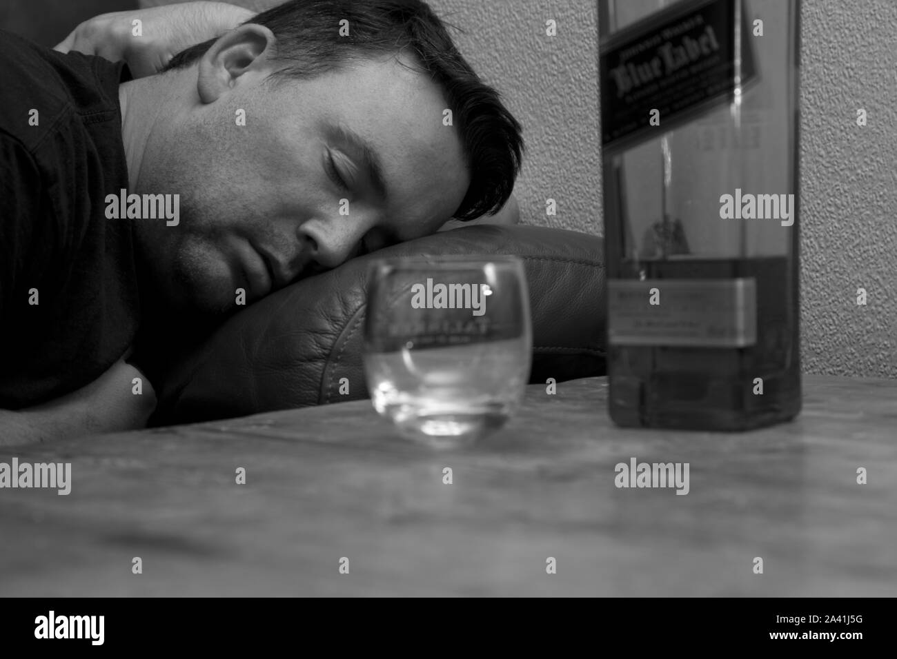 Un homme évanoui sur le canapé de dormir à côté d'une bouteille de whisky Johnnie Walkers étiquette bleue et un verre de whisky vide Banque D'Images