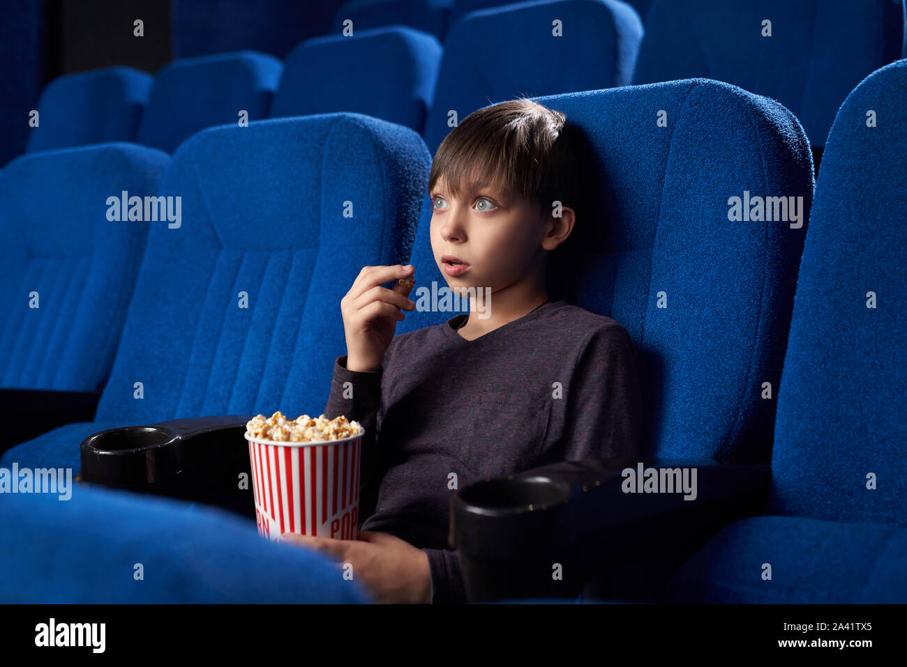 Voir du côté de l'heureux garçon aux grands yeux et bouche ouverte à regarder film incroyable dans le cinéma. Choqué male teen eating popcorn, regardant l'écran et de regarder l'horreur. Concept de loisir et de plaisir. Banque D'Images